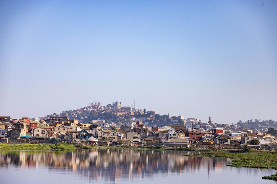 Houses on one of Antananarivo's hills reflected in still water under a clear sky
