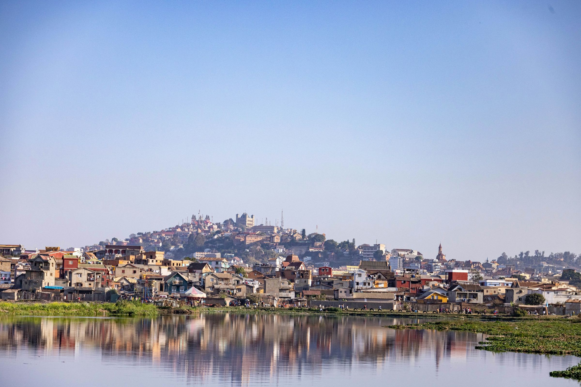 Houses on one of Antananarivo's hills reflected in still water under a clear sky