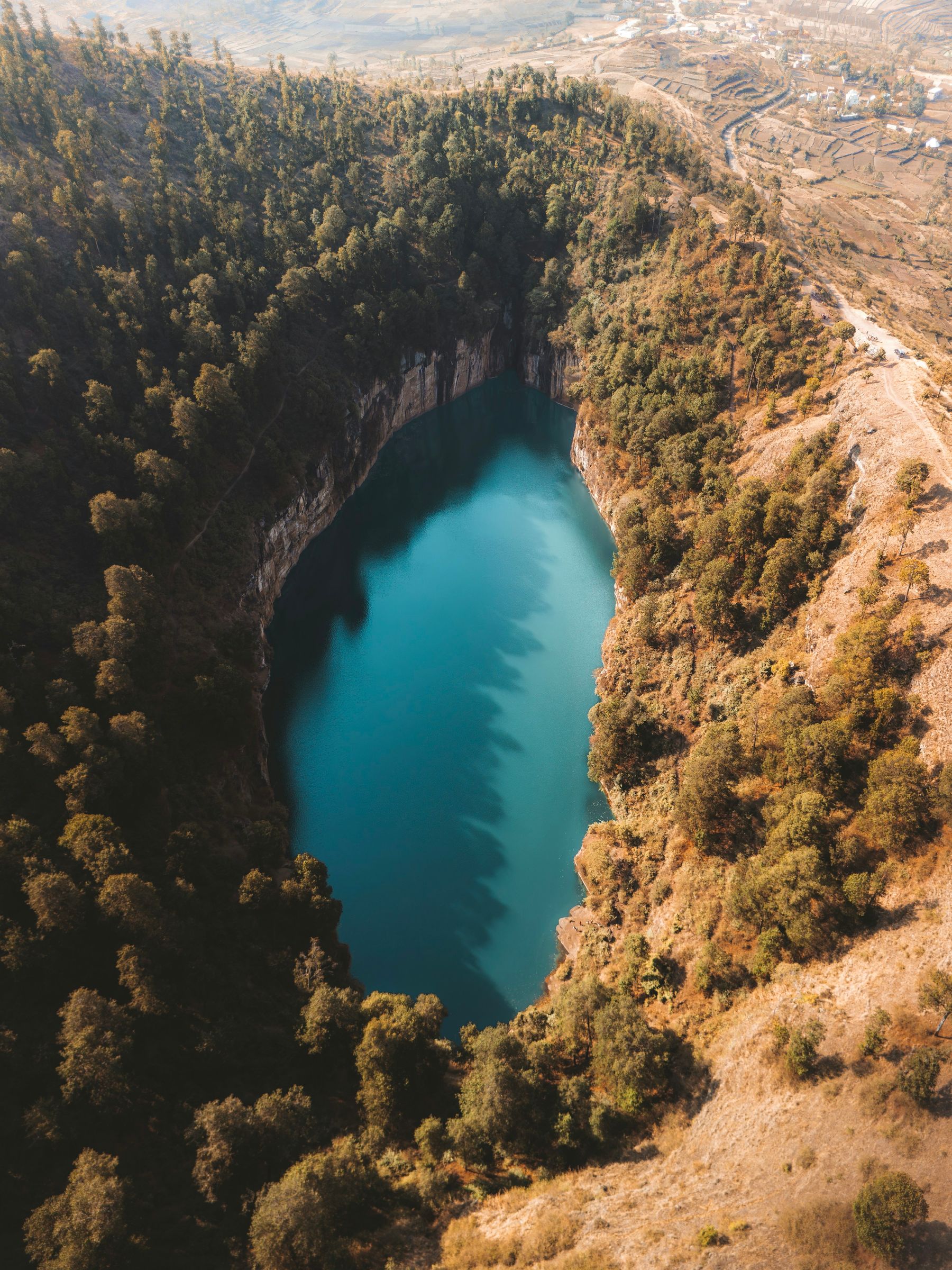 A deep blue crater lake ringed by cliffs and pine trees, seen from the air near Antsirabe