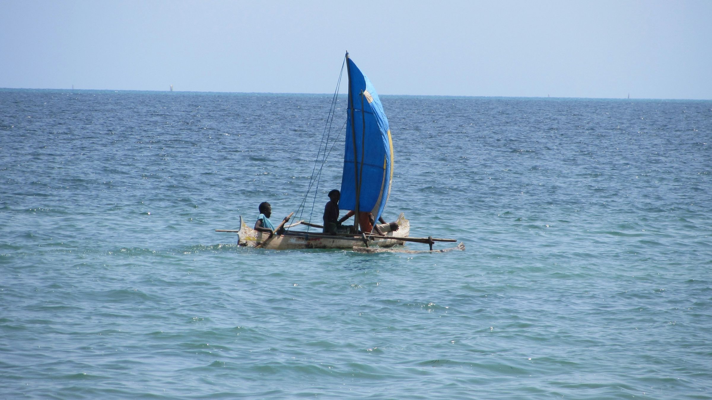 An outrigger pirogue with a blue sail on the sea off Ifaty