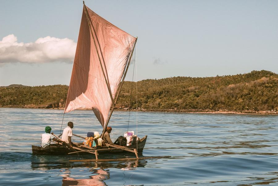 An outrigger sailing pirogue with passengers on a calm bay near Nosy Be