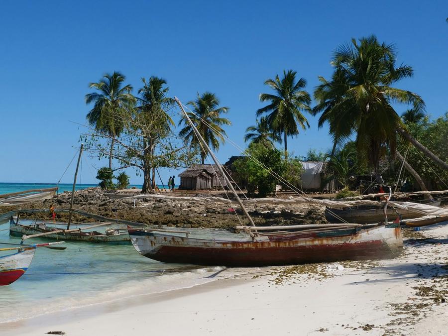 Wooden sailing boats pulled up on a white beach below palms and huts on Nosy Iranja