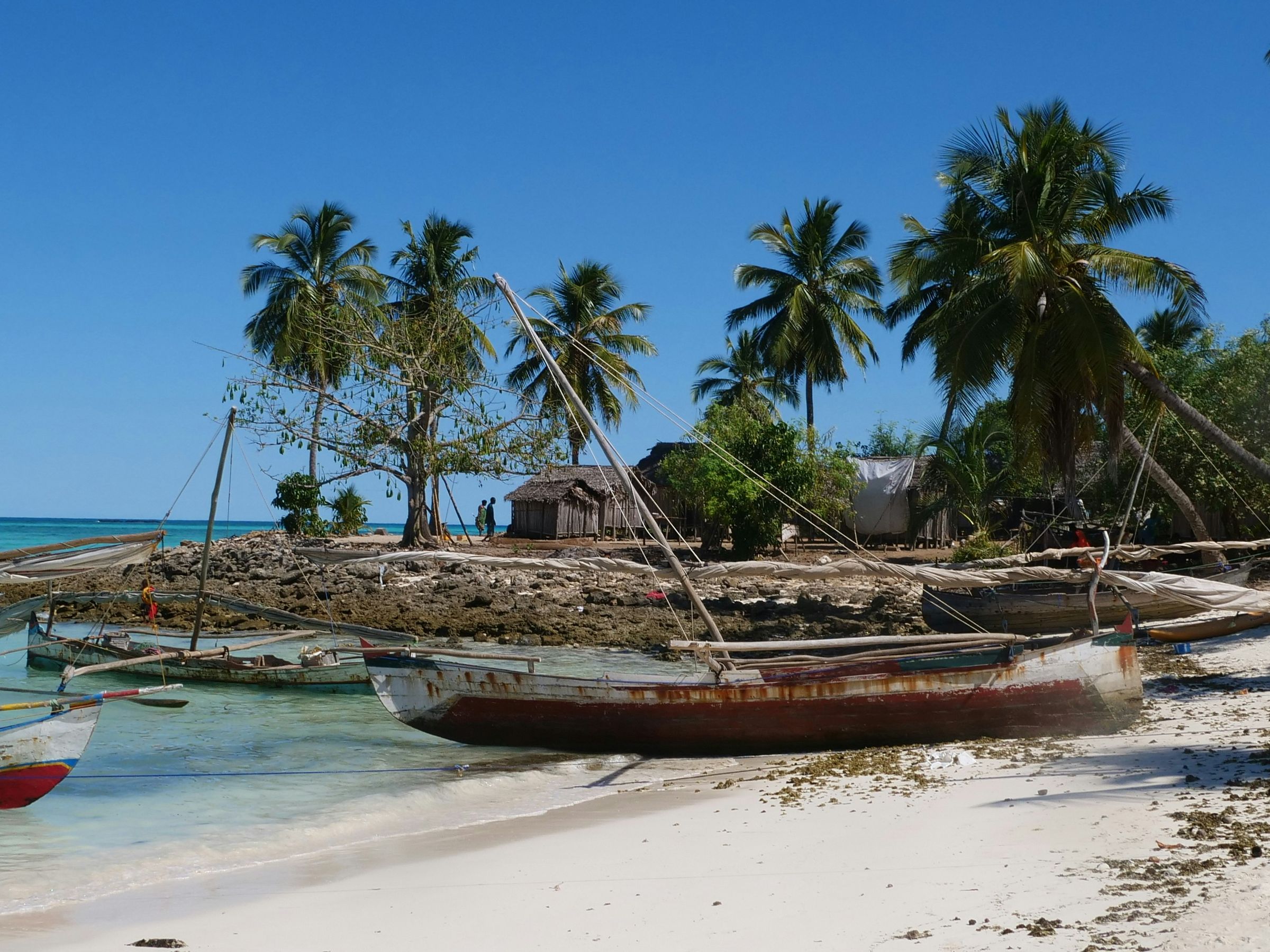 Wooden sailing boats pulled up on a white beach below palms and huts on Nosy Iranja