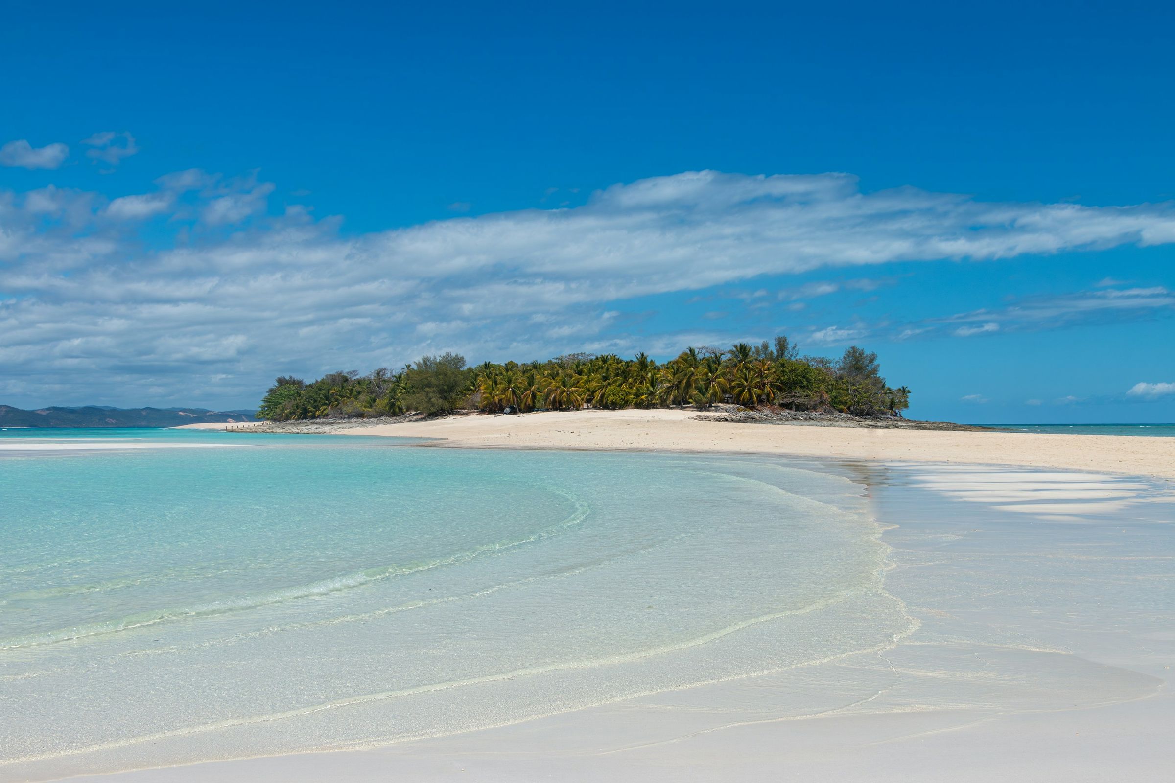 Clear shallow water and the white sandbar running out to a small island of palms at Nosy Iranja
