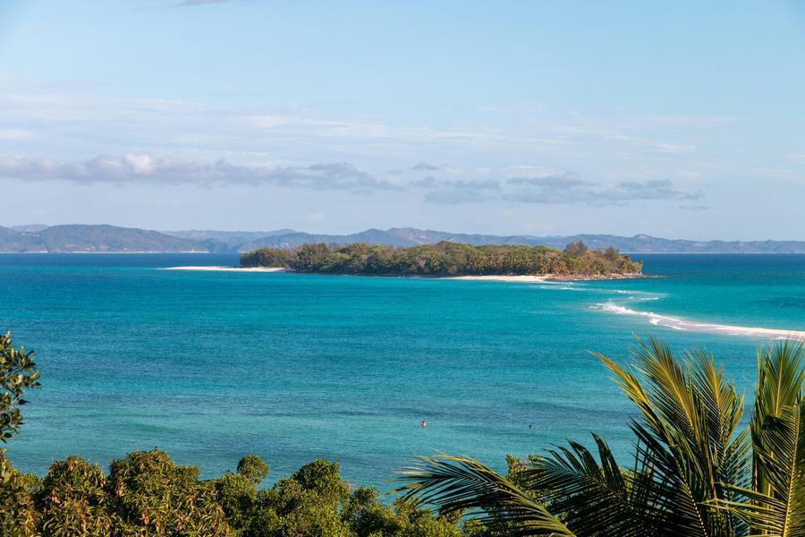 Turquoise sea and a small wooded island with a sandbar, seen from a hill on Nosy Iranja