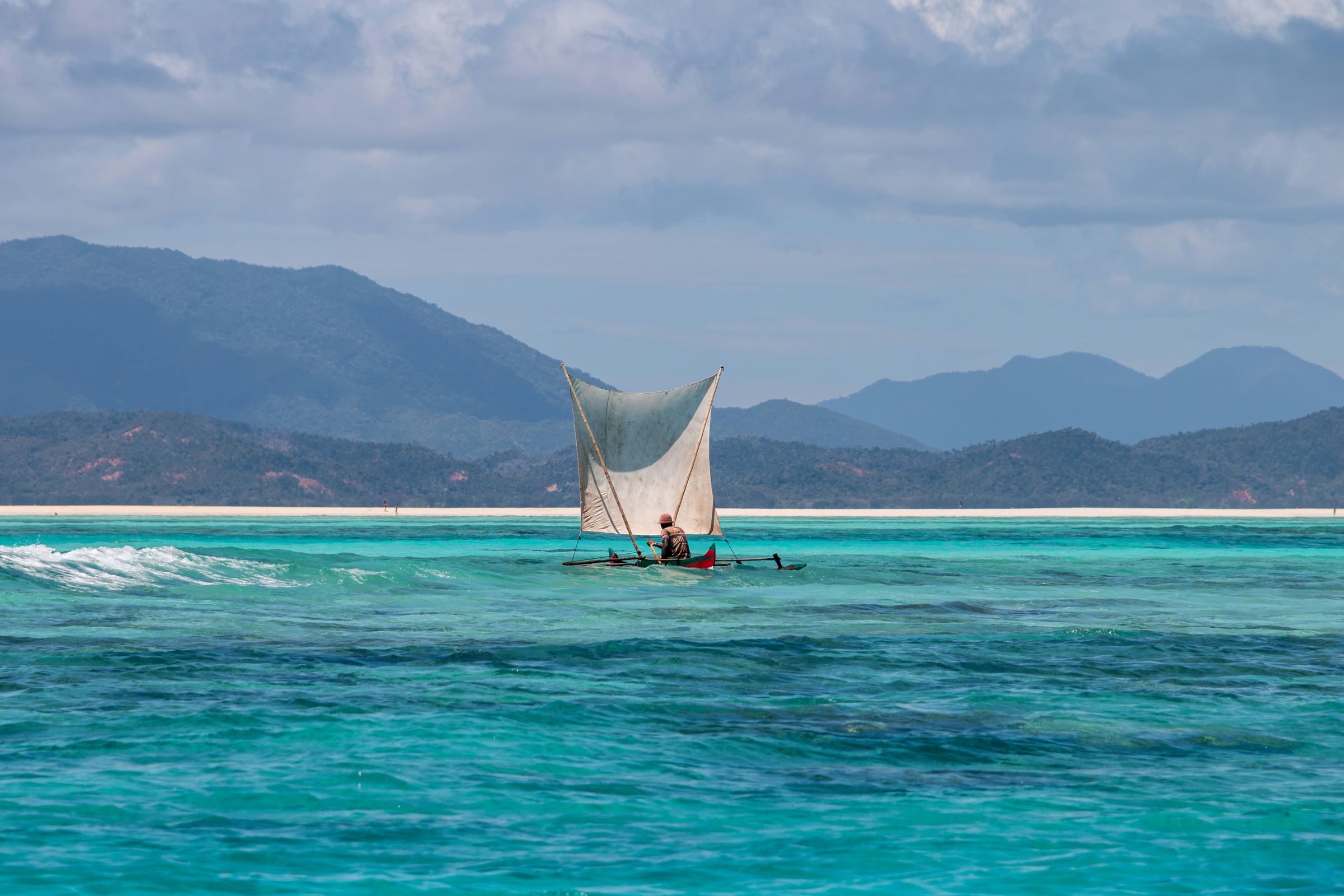 A fisherman sailing a pirogue over turquoise water near Nosy Iranja
