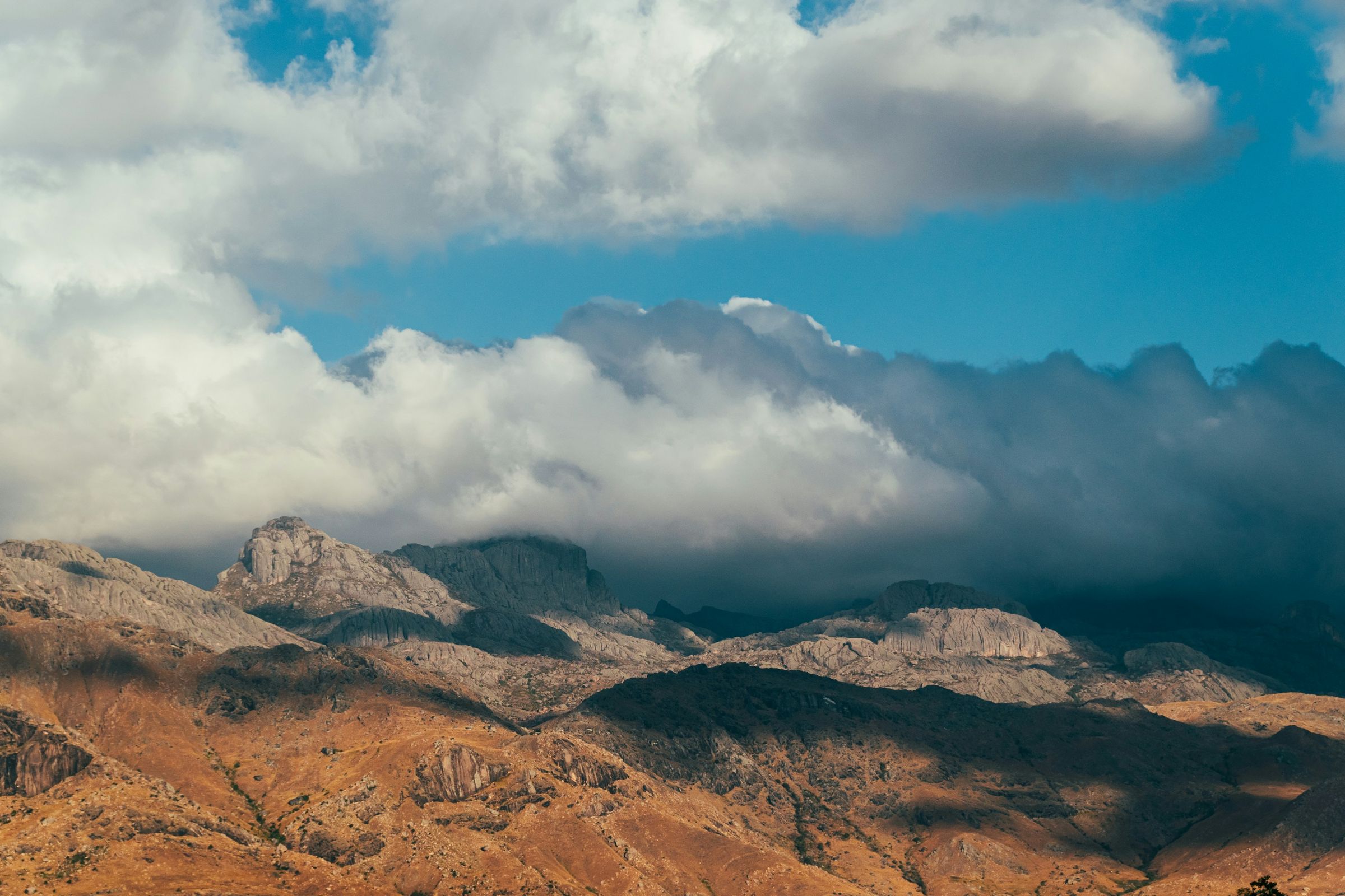 Granite peaks half hidden by heavy cloud above dry golden slopes, seen from Camp Catta in the Tsaranoro valley