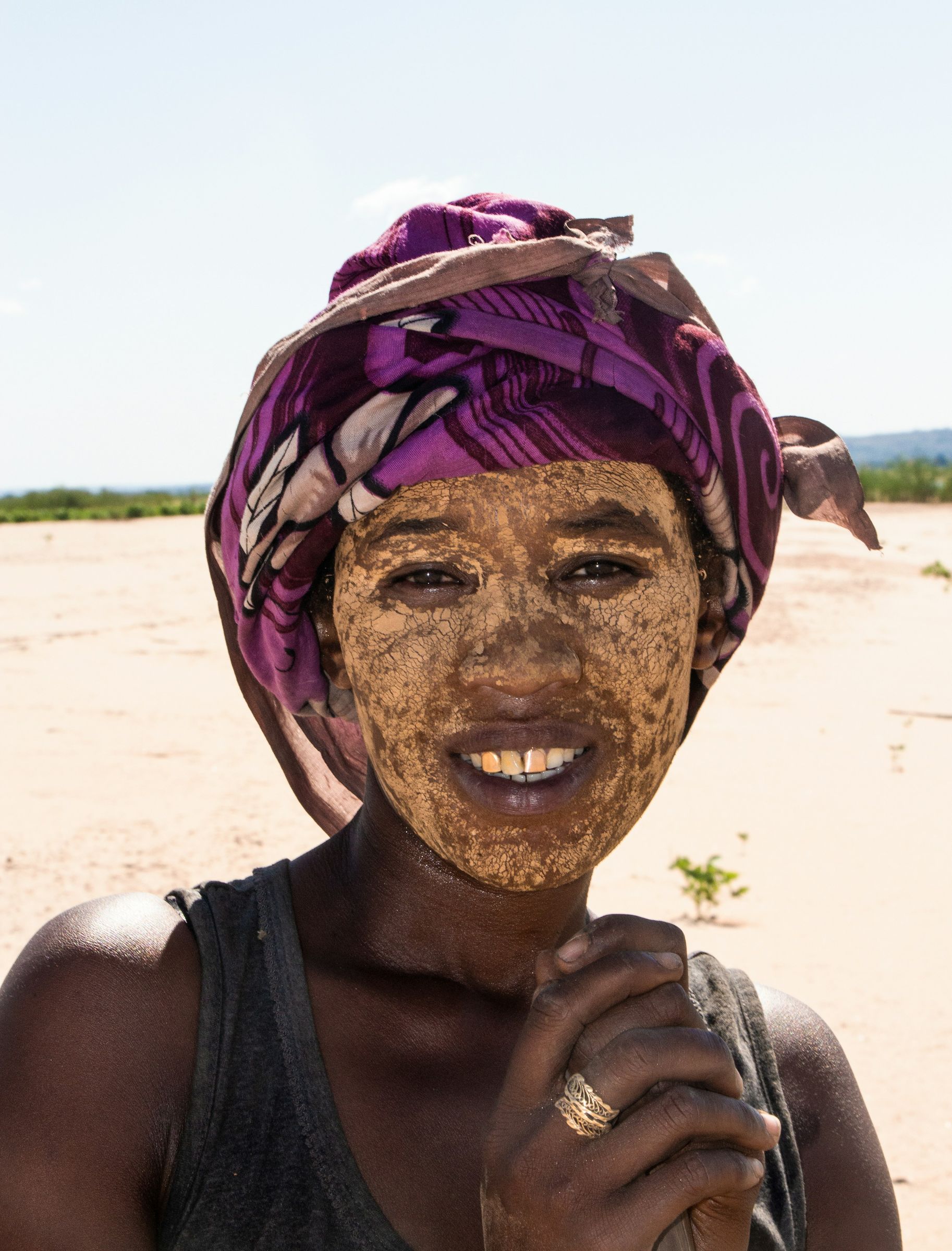 A woman in a purple headscarf, her face covered in a pale paste, by the Tsiribihina River